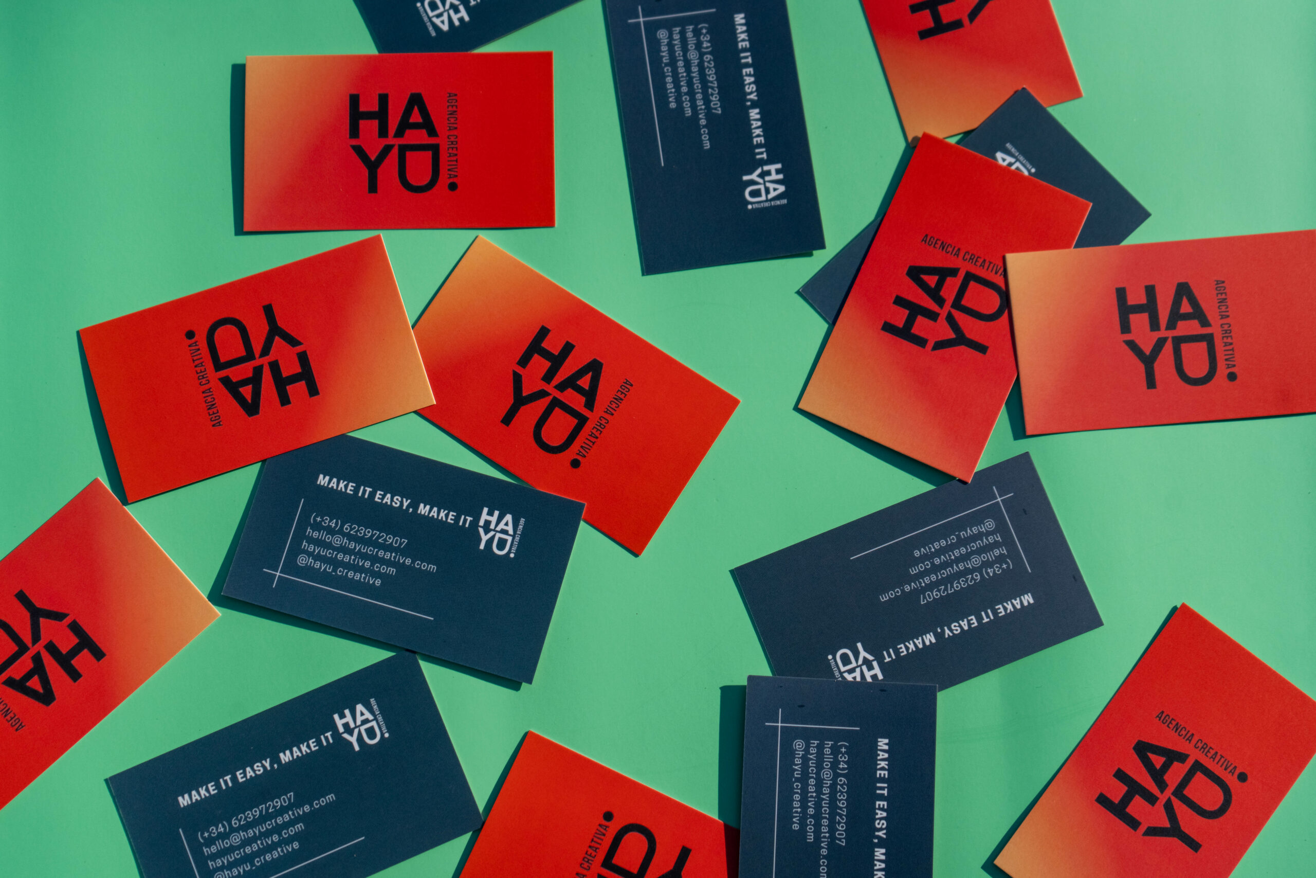 Tarjetas de visita naranjas y azul marino de Hayu Creative sobre fondo verde